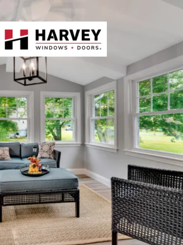 Bright sunroom with large Harvey double-hung windows, wicker chairs, and an ottoman with flowers.