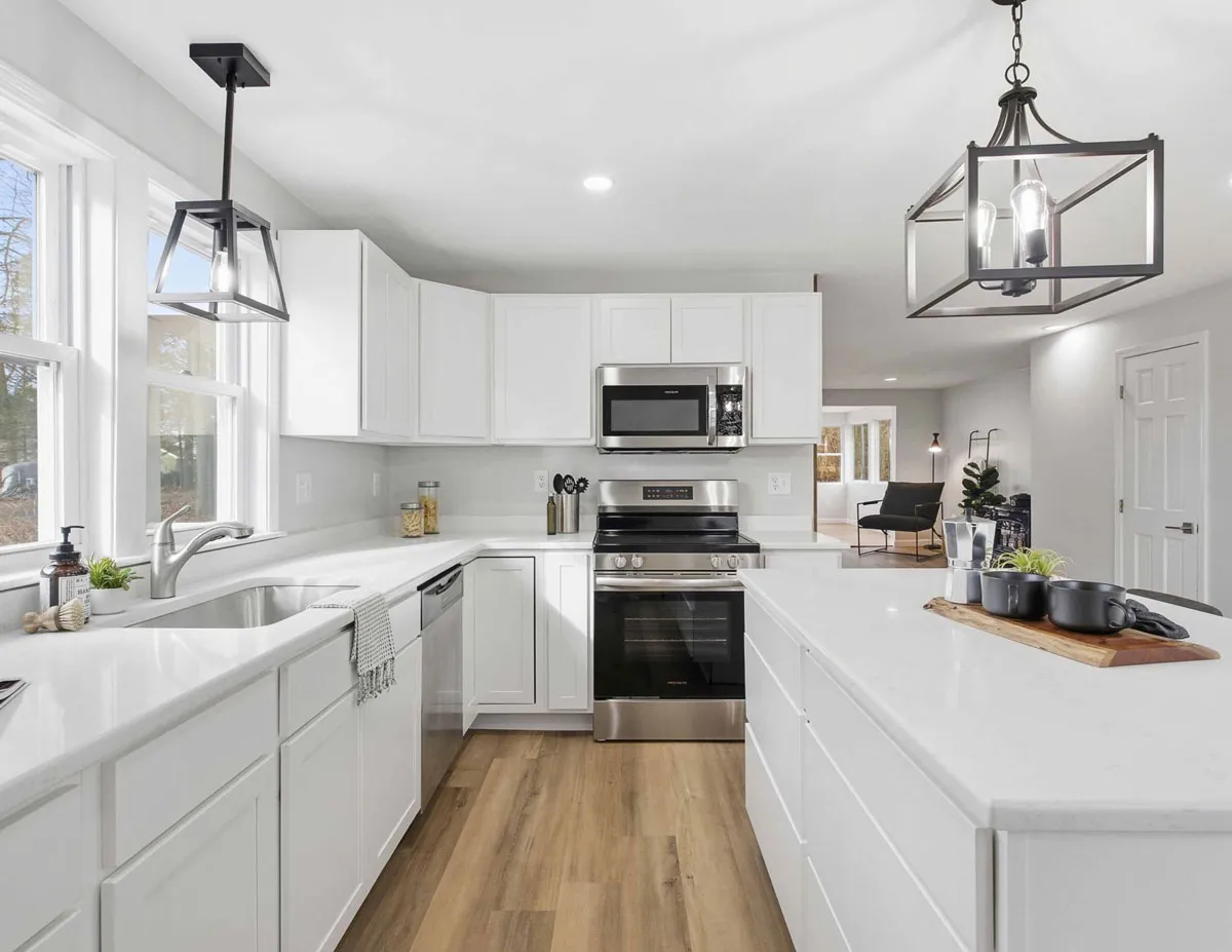 Modern white kitchen with stainless steel appliances and wooden floor, featuring an island with decor.