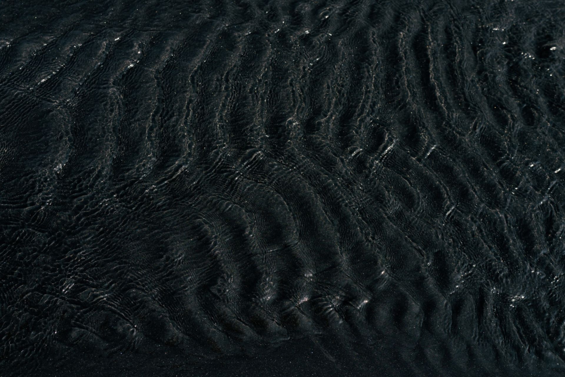 Wellenförmige Rippeln in dunklem Sand