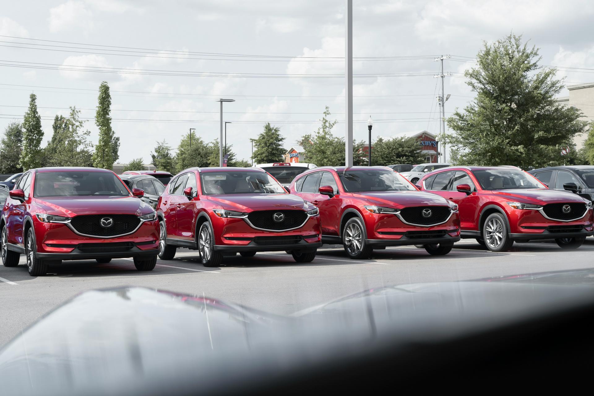 Four red Mazda CX-5 SUVs parked in a row in an outdoor parking lot on a cloudy day.