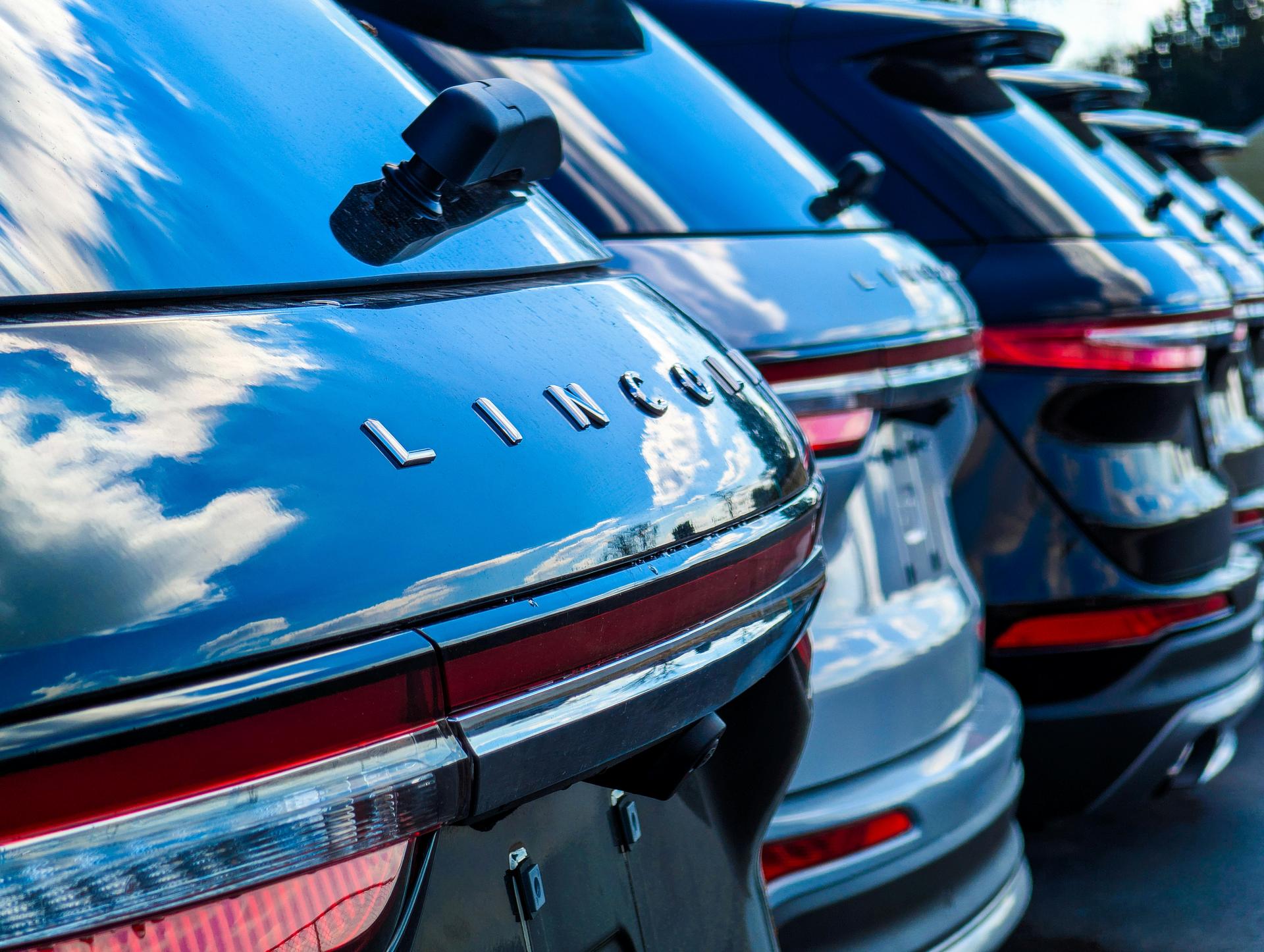 Row of Lincoln SUVs parked closely, focusing on the shiny rear ends with reflections of clouds on the surface.