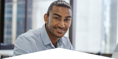 Smiling young man with tied-back hair wearing a light blue shirt in an office setting.