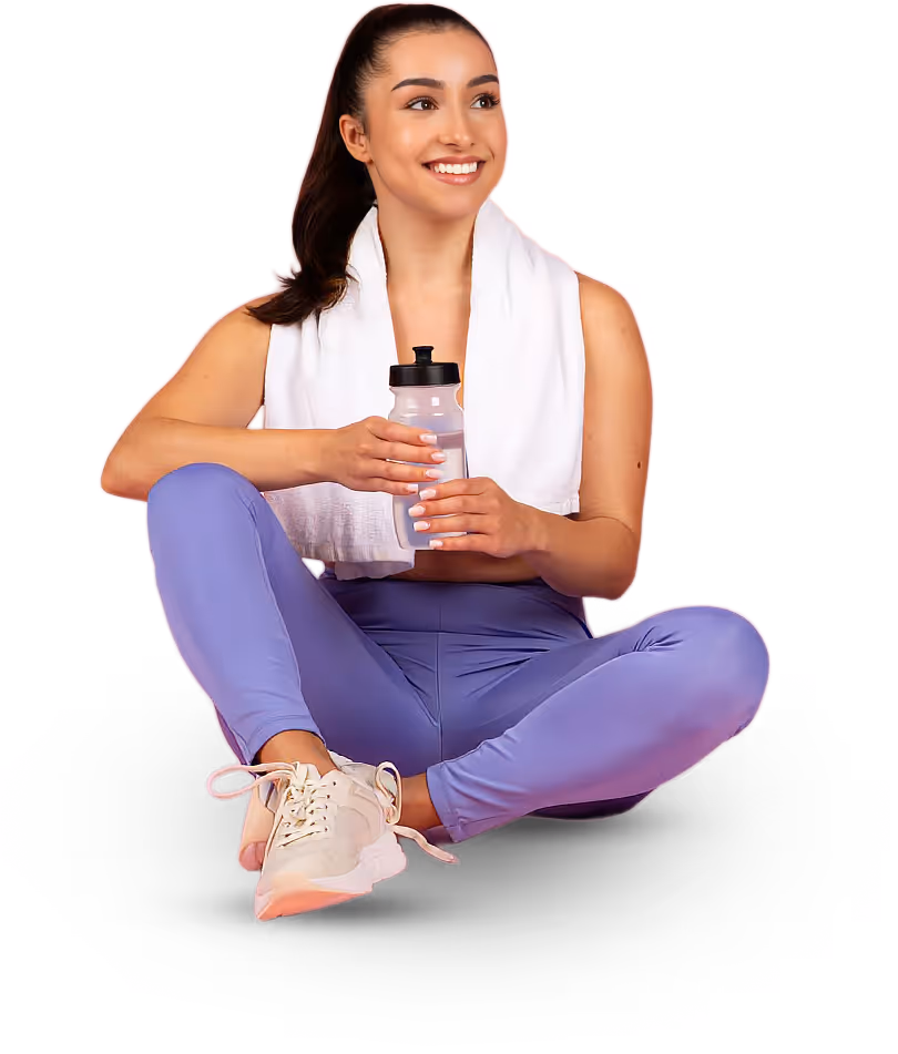 Smiling woman in purple leggings and white sneakers sitting cross-legged with a white towel around her neck, holding a water bottle.