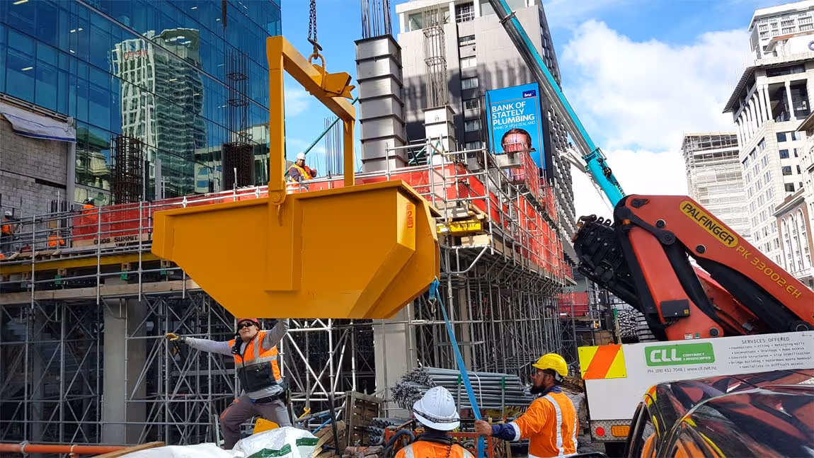 Construction workers on site guiding a large yellow metal container being lifted by a crane in an urban building project.