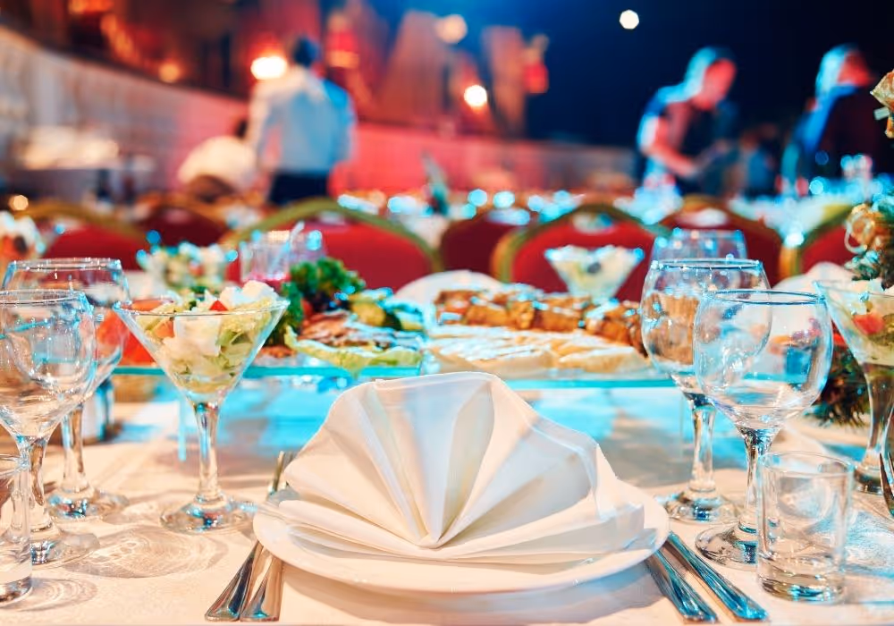 Eleganter gedeckter Tisch mit gefaltetem weißen Servietten, Gläsern und Salatgläsern bei einer festlichen Veranstaltung.