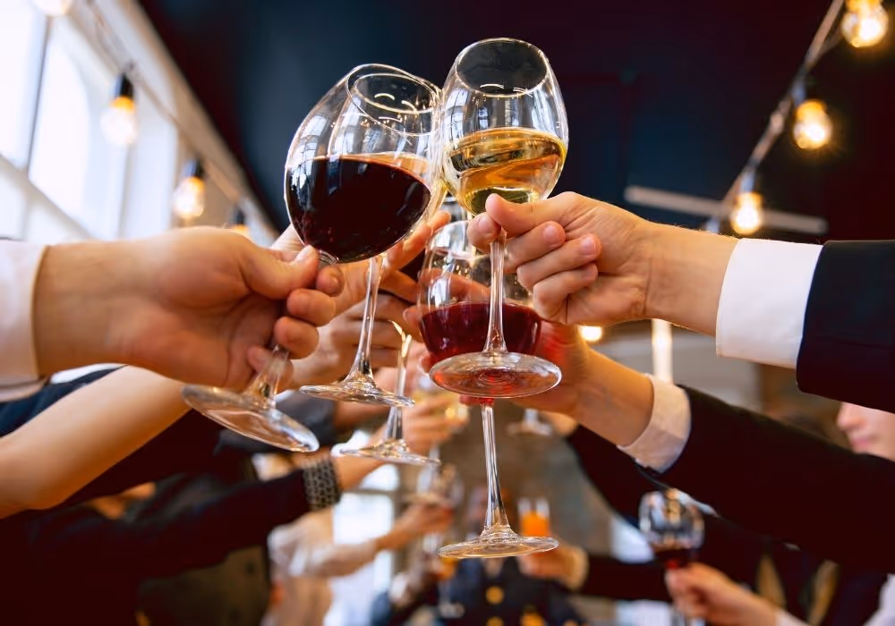 Menschen stoßen mit Weingläsern gefüllt mit rotem und weißem Wein in einem festlichen Ambiente an.