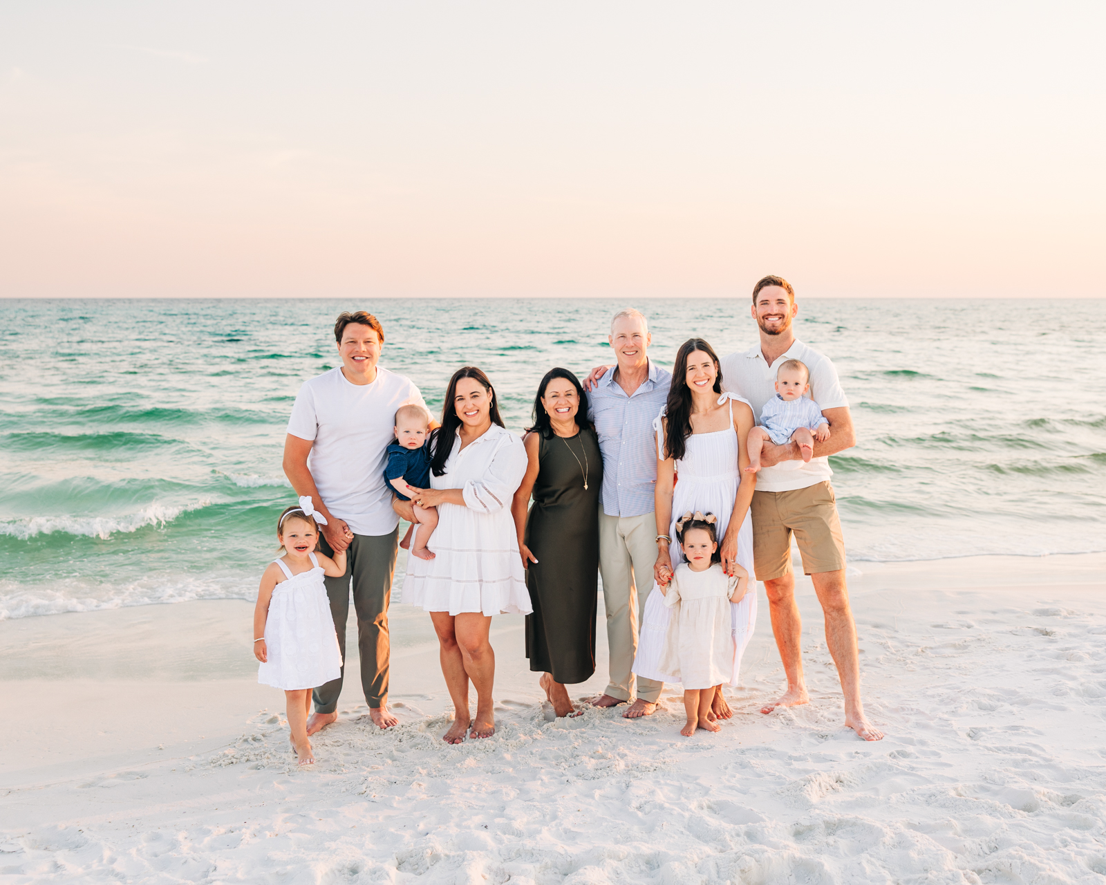 Multi-generational family in white and neutral outfits grouped together on 30A beach at sunset