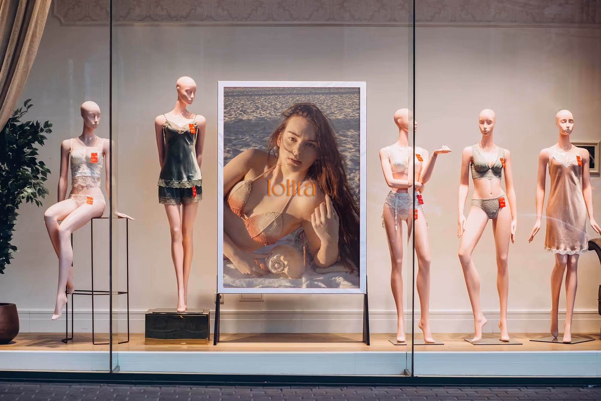 Store window with five female mannequins dressed in lingerie around a poster of a woman on a beach.