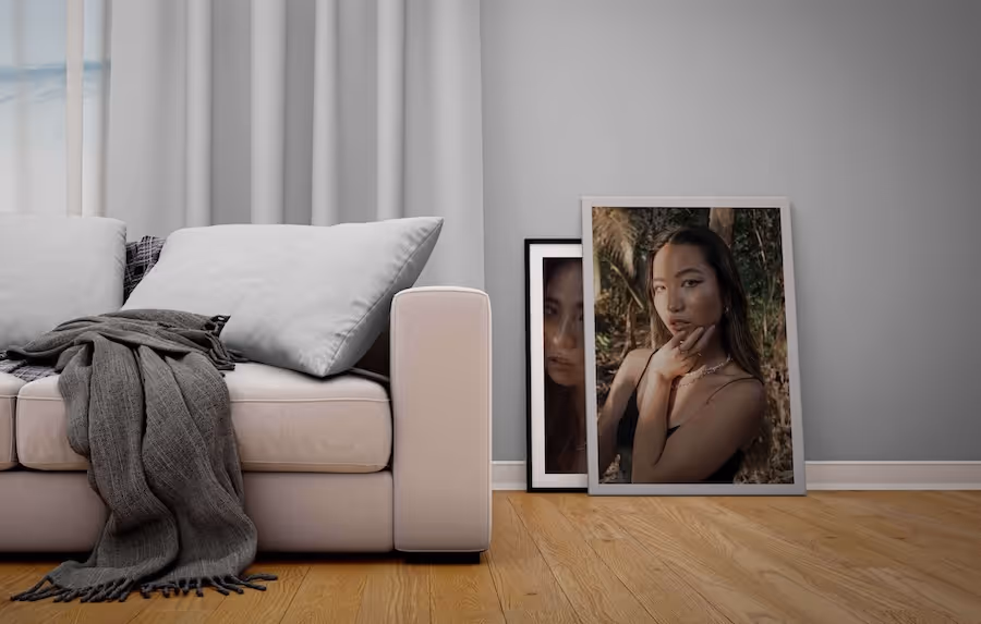 Light sofa with cushions and grey throw next to two framed photos of a woman on a wooden floor.