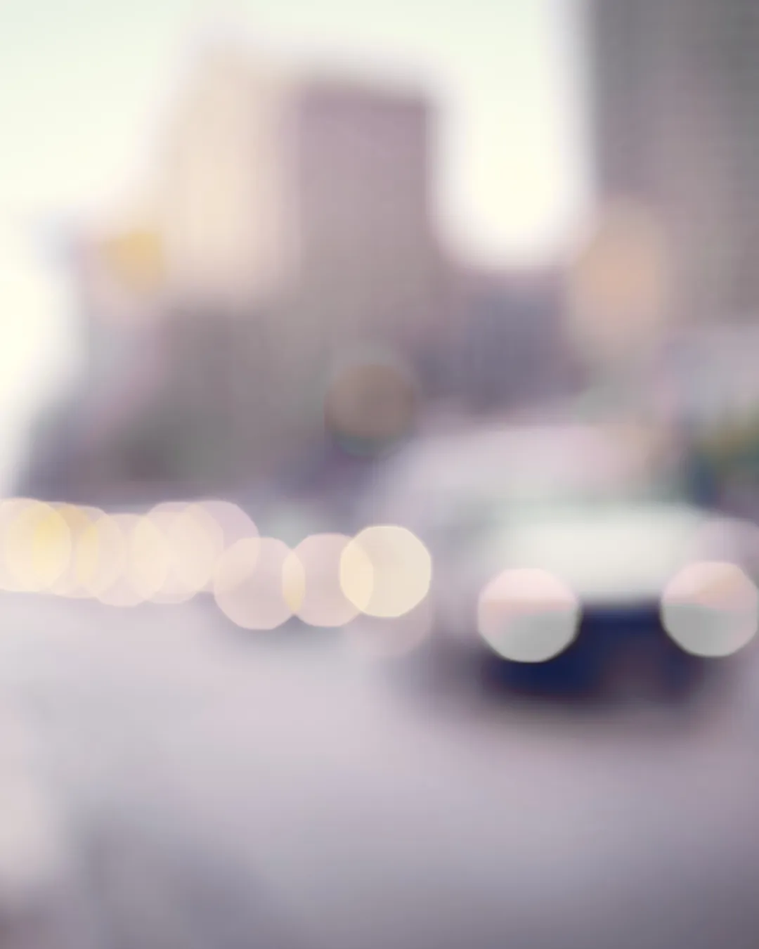 Blurred city street scene with car headlights and tall buildings in the background.