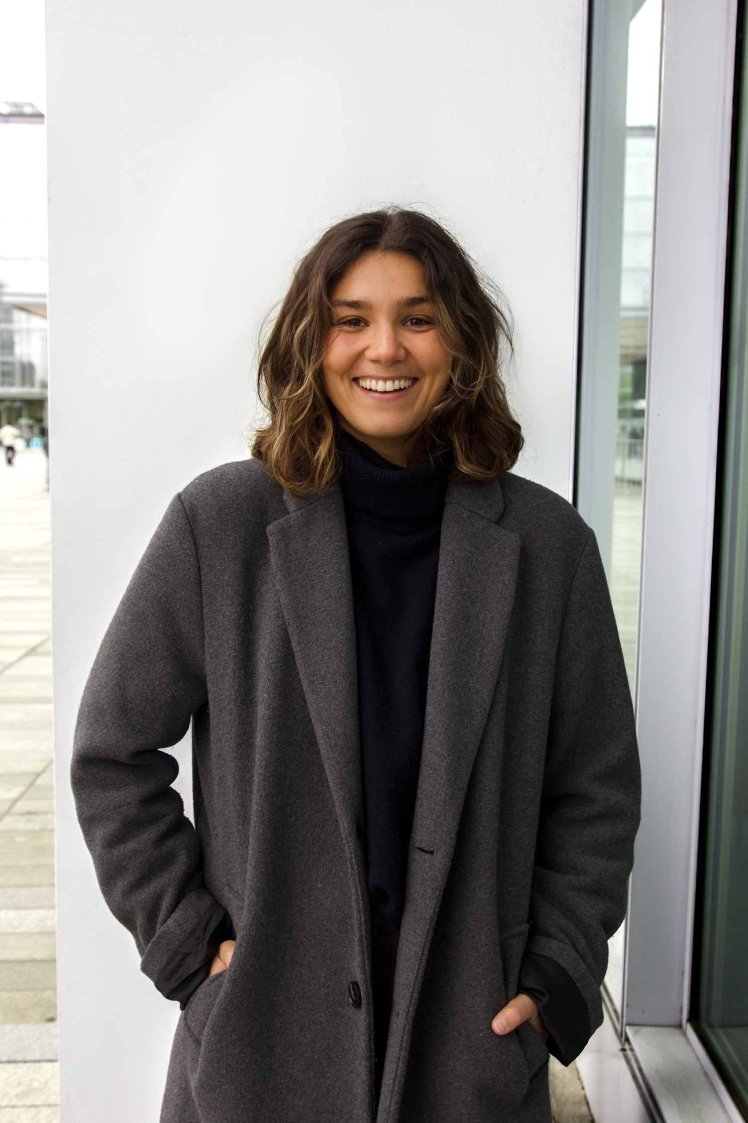 Black and white photo of a woman in a white blazer looking back with a blurred background of a grid window and textured wall.