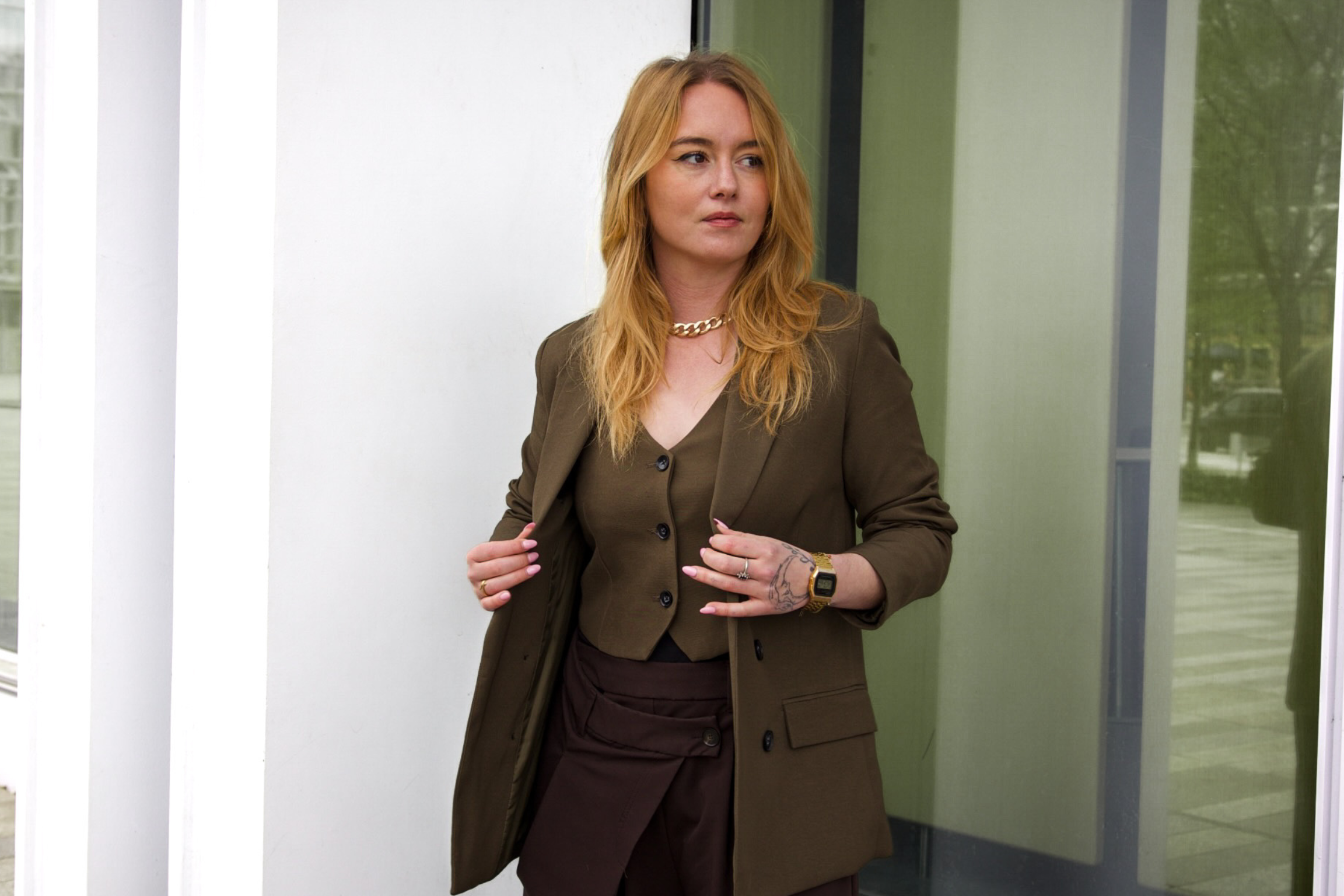 Black and white photo of a woman in a white blazer looking back with a blurred background of a grid window and textured wall.