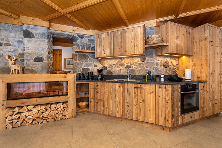 Rustic kitchen with wooden cabinets, stone walls, built-in fireplace with stacked firewood, and modern appliances including a coffee maker and oven.
