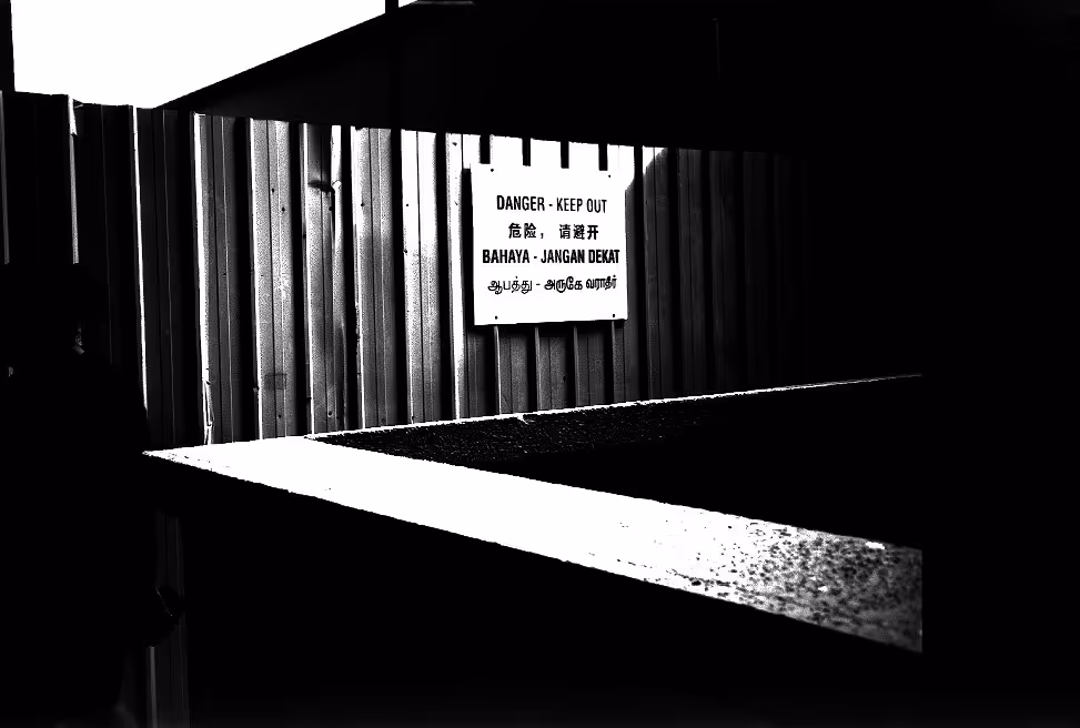 A harsh B&W film photo of an iconic sign found in Singapore, warning 'Keep Out!' in the four major dialects.