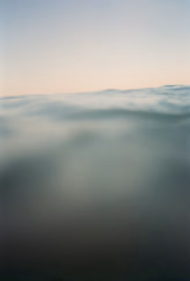 A semi-underwater film photo of a distant horizon above a blurry ocean touching the camera lens.