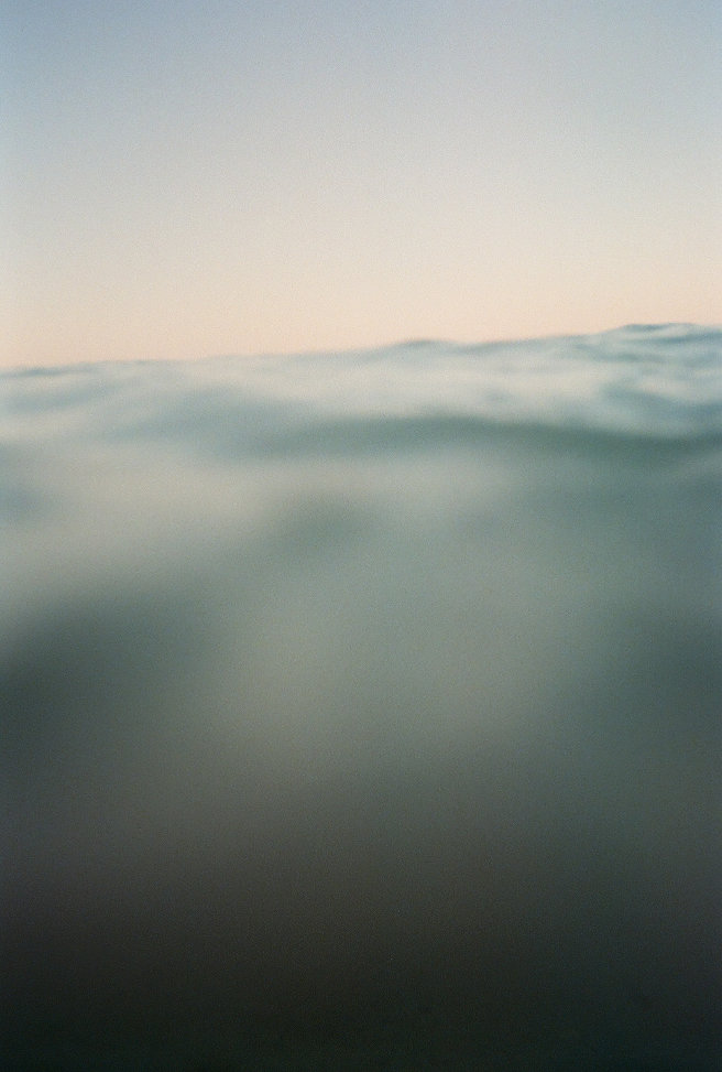 A semi-underwater film photo of a distant horizon above a blurry ocean touching the camera lens.