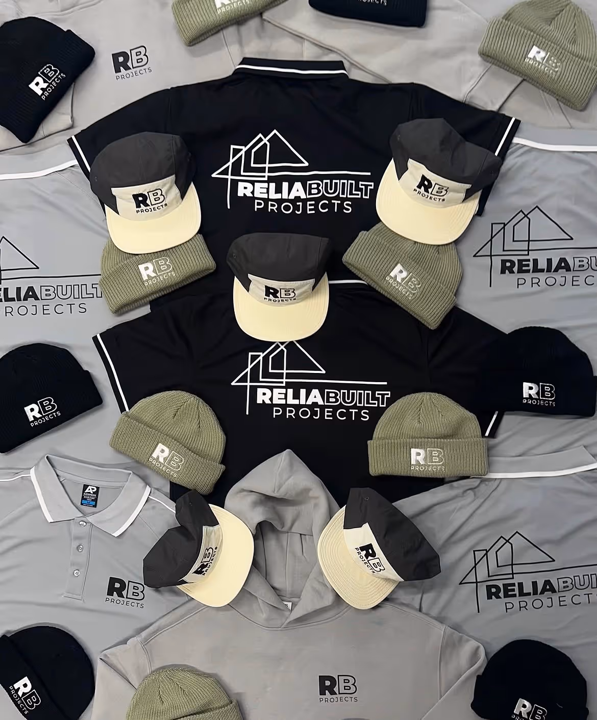 Flat lay of black and gray apparel including polo shirts, hoodies, caps, and beanies all branded with RB Projects logo.