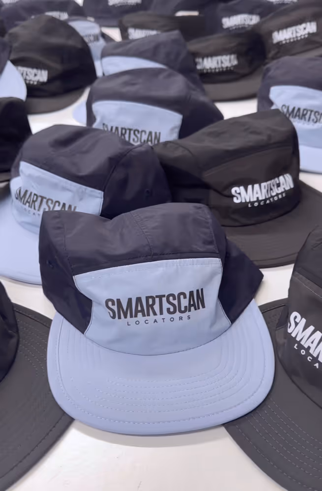 Multiple black and gray caps with Smartscan Locators logo arranged on a white surface.