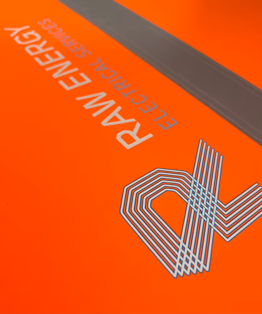 Close-up of orange surface with Raw Energy Electrical Services text and line art logo design.