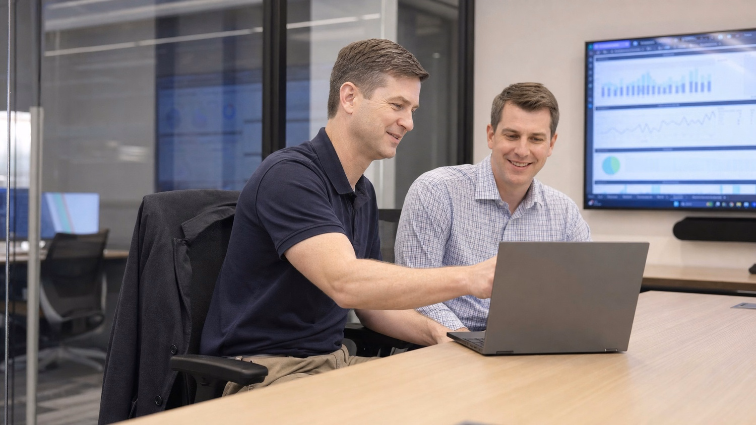 Man in polo reviews laptop screen with colleague