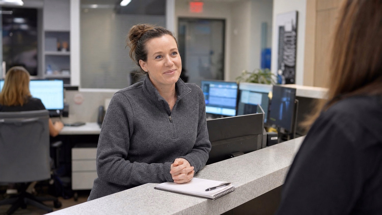 Receptionist greets visitor at modern office desk, notebook ready 71 chars