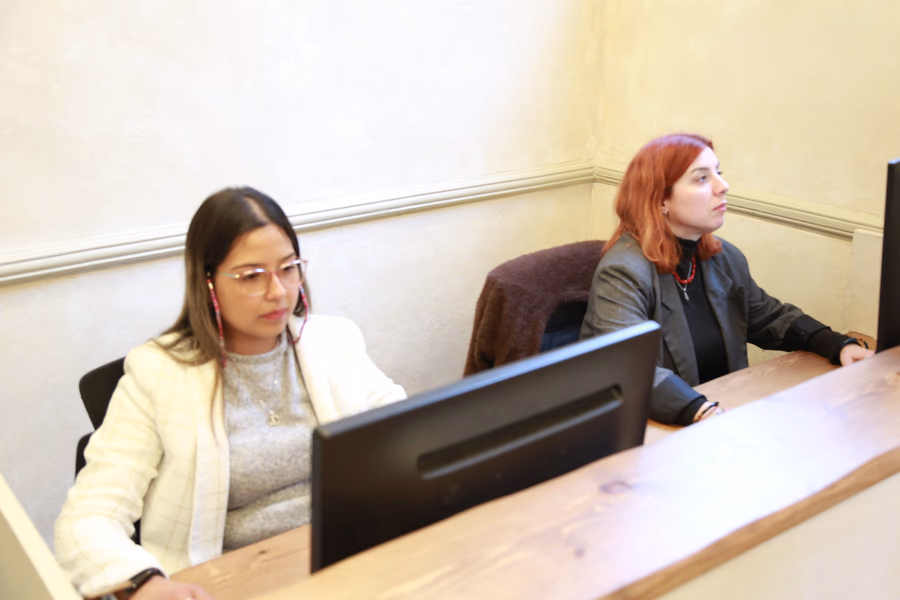 Two women working at separate desks with computers in an office setting.