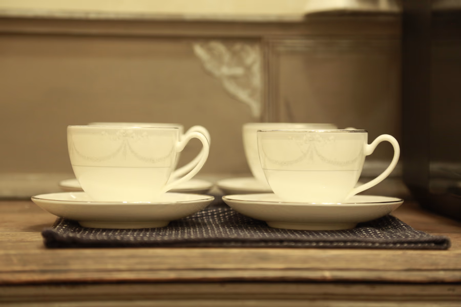 Four white porcelain teacups with saucers arranged on a dark cloth on a wooden surface.