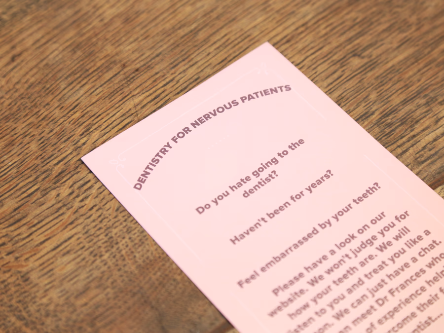 Pink pamphlet titled 'Dentistry for Nervous Patients' placed on a wooden surface.
