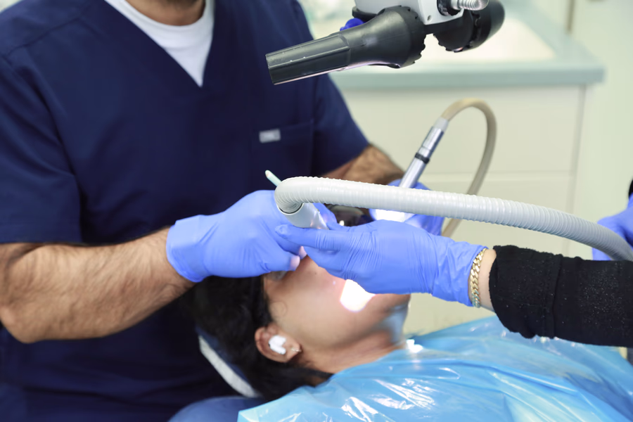 Dentist and assistant wearing blue gloves performing a dental procedure on a patient lying on a chair.