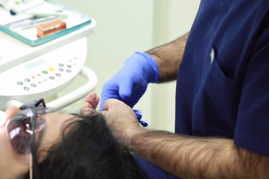 Dentist wearing blue gloves preparing dental tools for a patient wearing protective glasses.