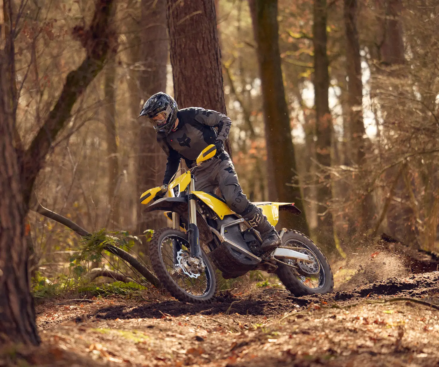 Person wearing black protective gear riding a yellow dirt bike on a muddy forest trail.