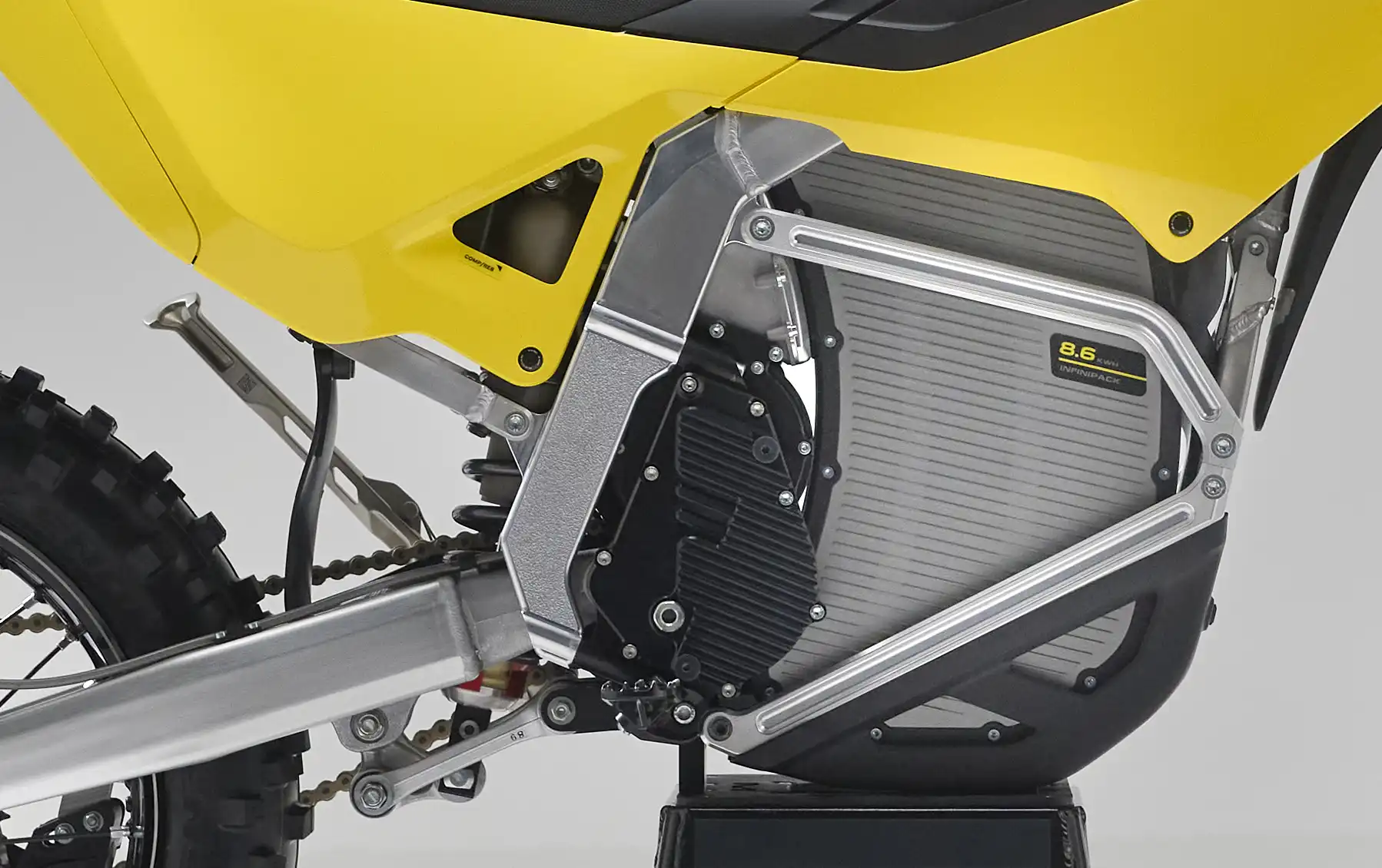Close-up of a yellow electric dirt bike's battery compartment and frame showing the 8.6 kWh Infinipack battery.