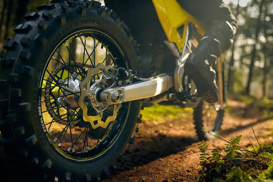 Close-up of a dirt bike rear wheel and suspension on a forest trail during golden hour.