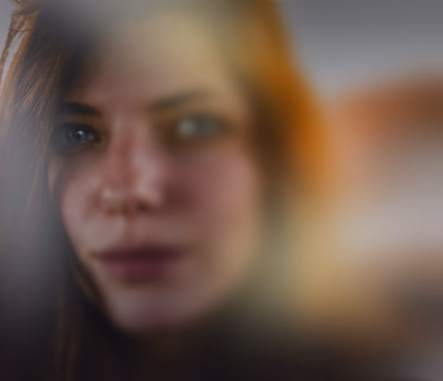 Blurred close-up of a woman's face with long hair and a neutral expression.