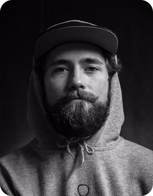 Portrait of a man with a beard wearing a hoodie and a cap in black and white.