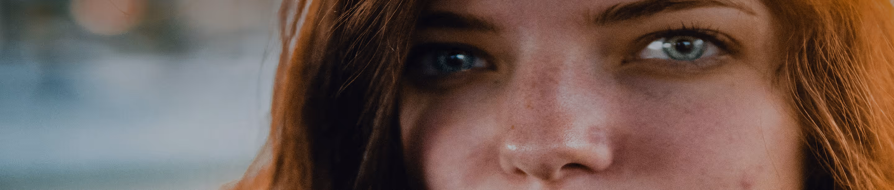 Close-up of a person's face showing green eyes, freckles, and red hair.