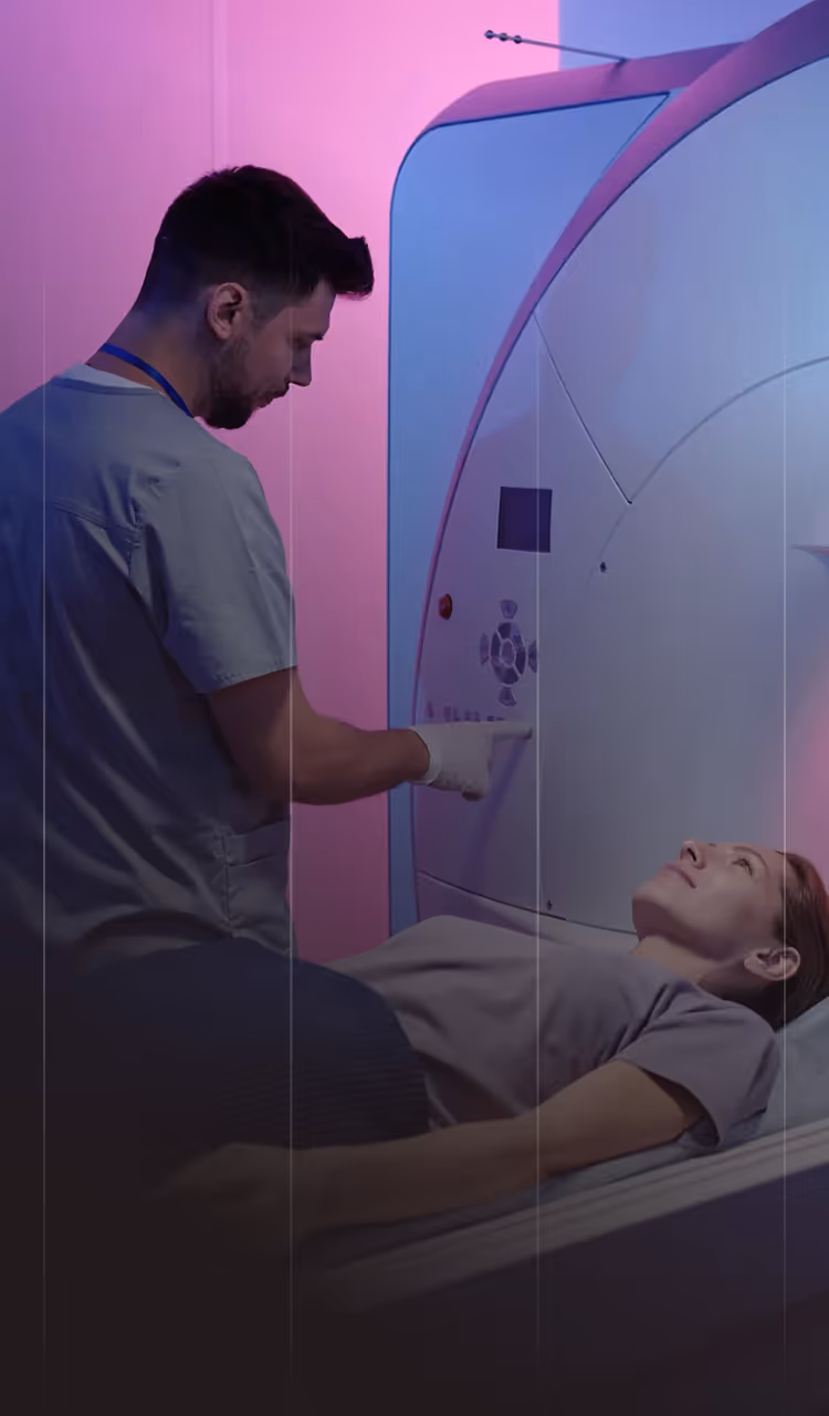 Medical professional operating MRI machine while patient lies on the scanner bed.