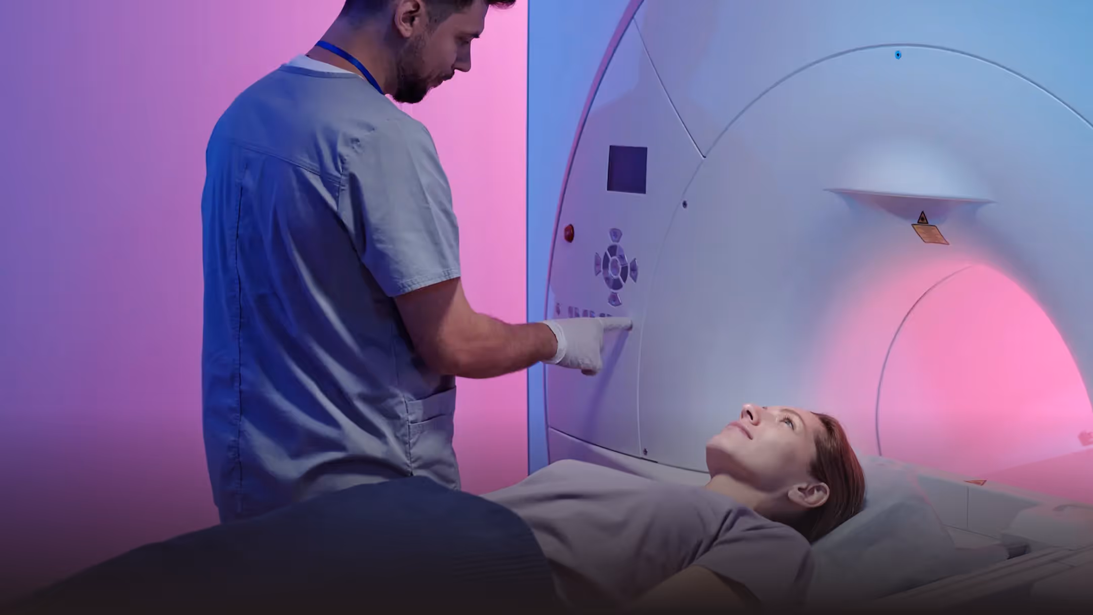 Medical professional operating an MRI machine while a patient lies on the scanning table inside the machine.