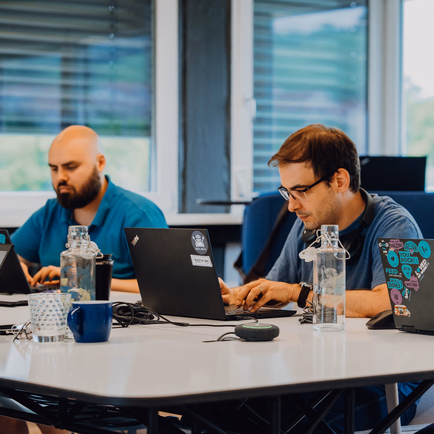 Two men working on laptops at a conference table.