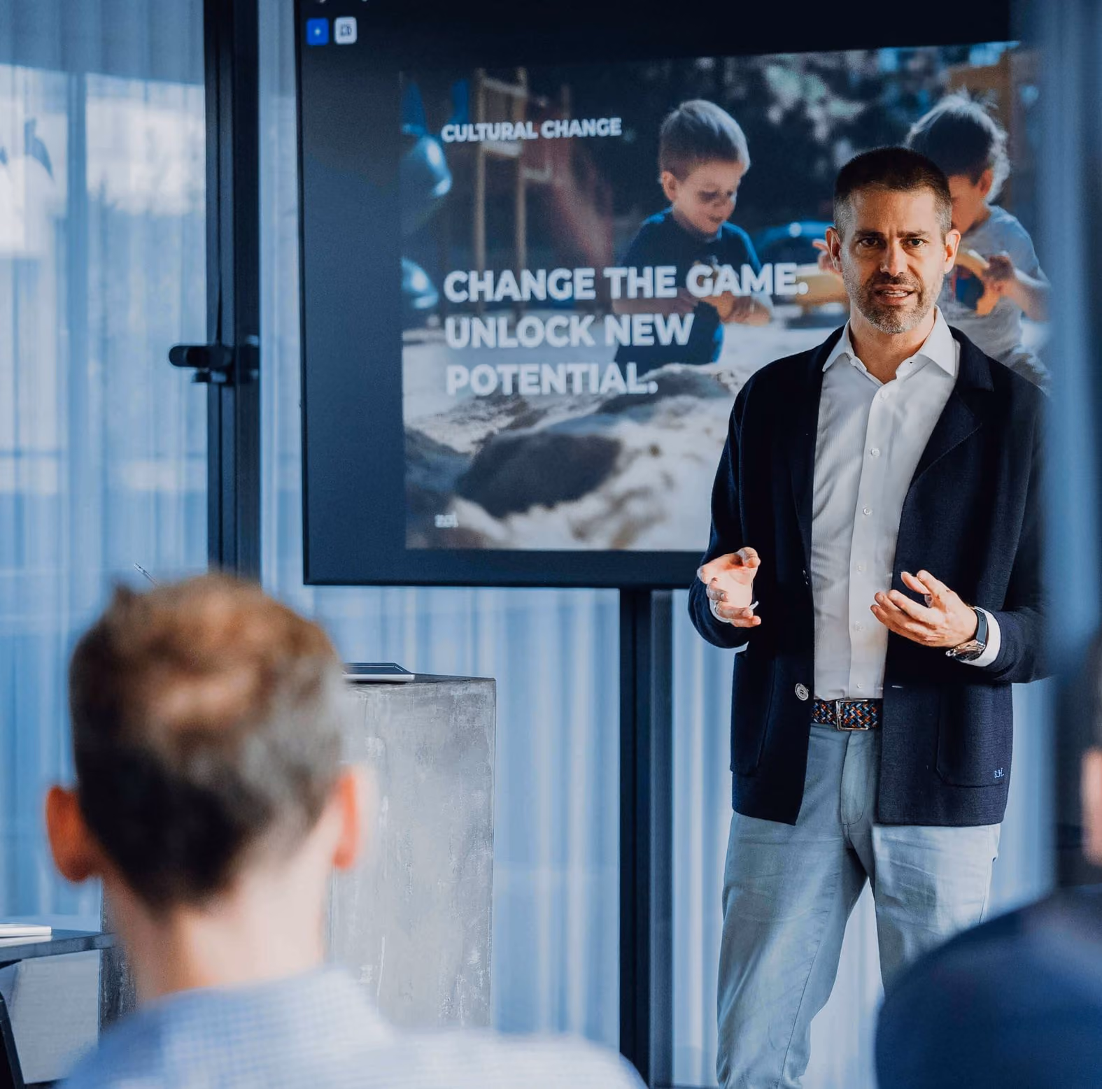 Man giving a presentation in front of a screen showing children and text about unlocking new potential.