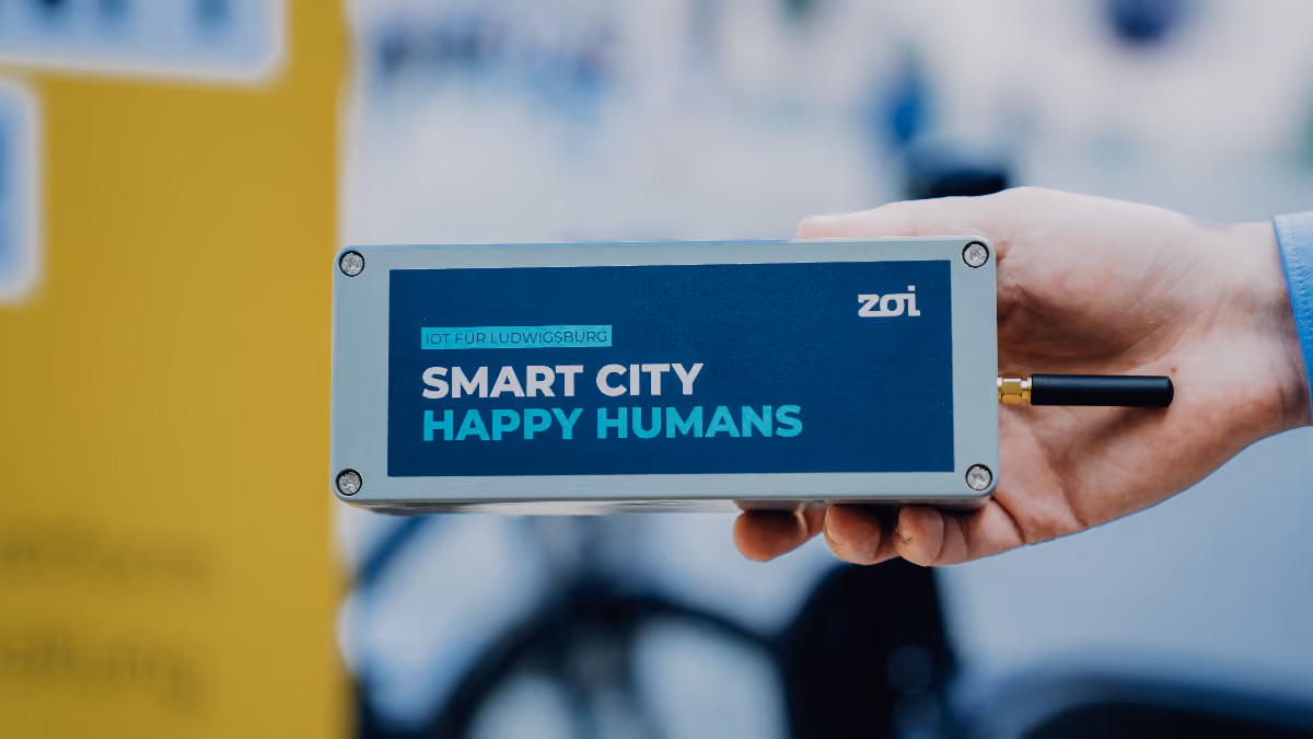 Hand holding a device labeled 'Smart City Happy Humans' with a small antenna attached.