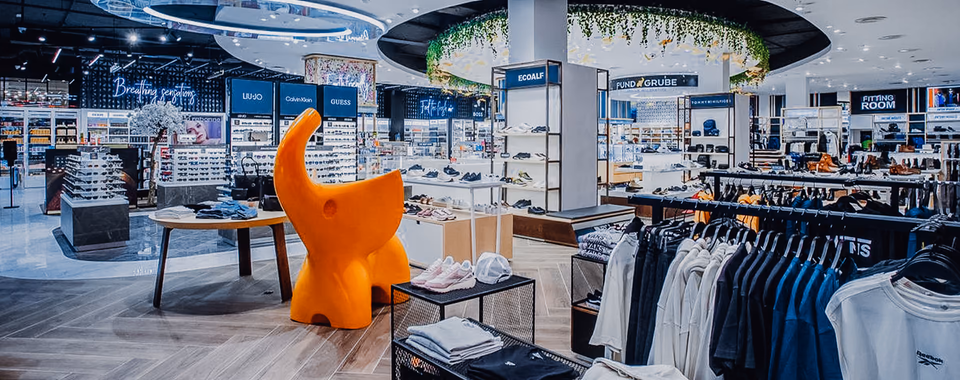 Modernes Einzelhandelsgeschäft mit Kleiderständern, Schuhdisplays, Markenschildern und einer orangefarbenen Elefantenskulptur.