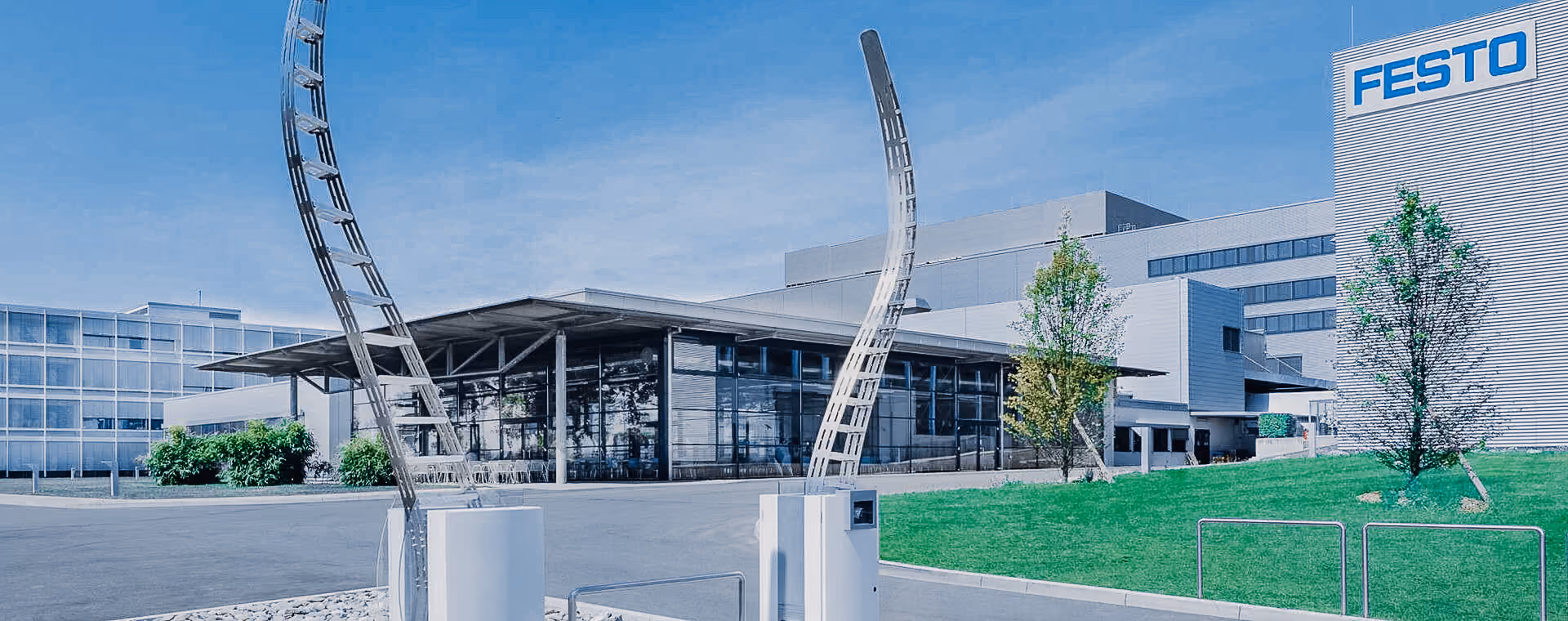 Modernes Industriegebäude mit großen Glasfenstern, Metallskulptur, grünem Rasen und Festo-Logo an der Wand.