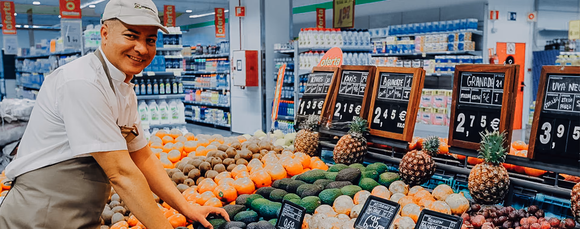 Lächelnder Angestellter eines Lebensmittelgeschäfts, der Avocados und andere Früchte in der Obst- und Gemüseabteilung arrangiert.