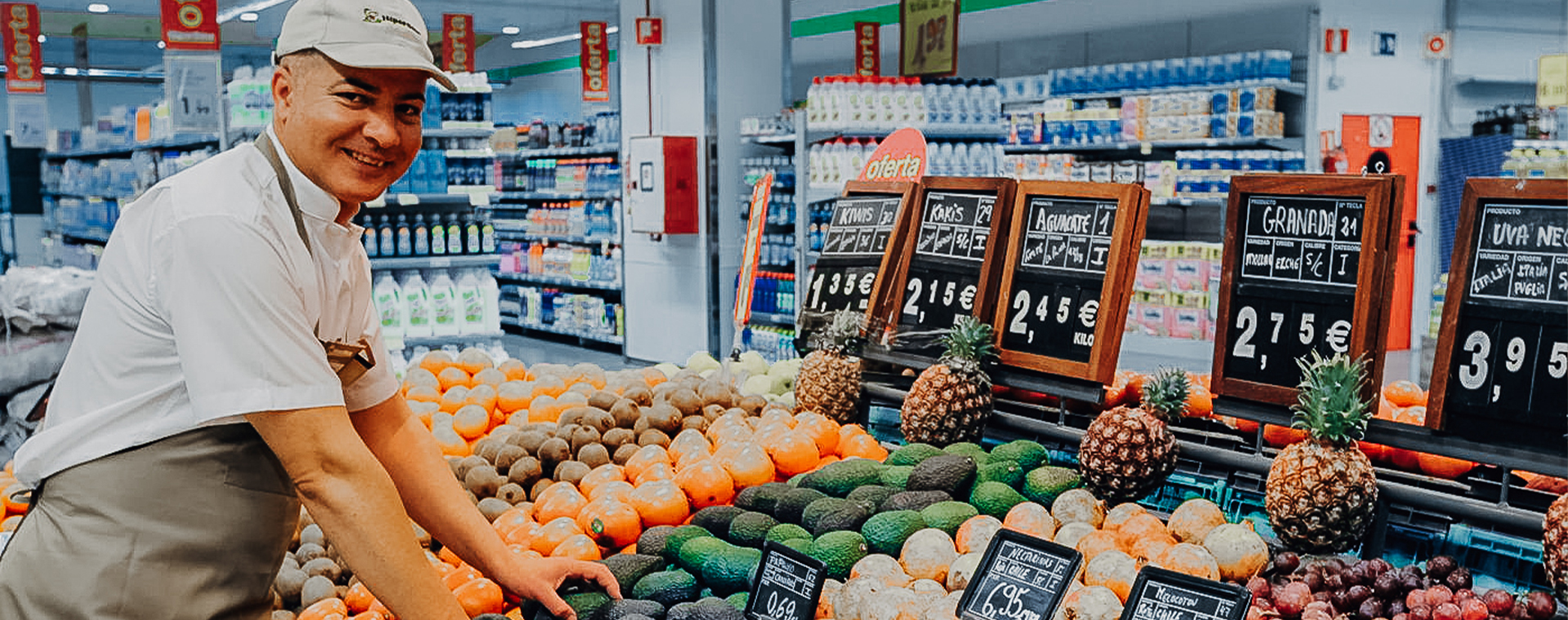 Lächelnder Angestellter eines Lebensmittelgeschäfts, der Avocados und andere Früchte in der Obst- und Gemüseabteilung arrangiert.