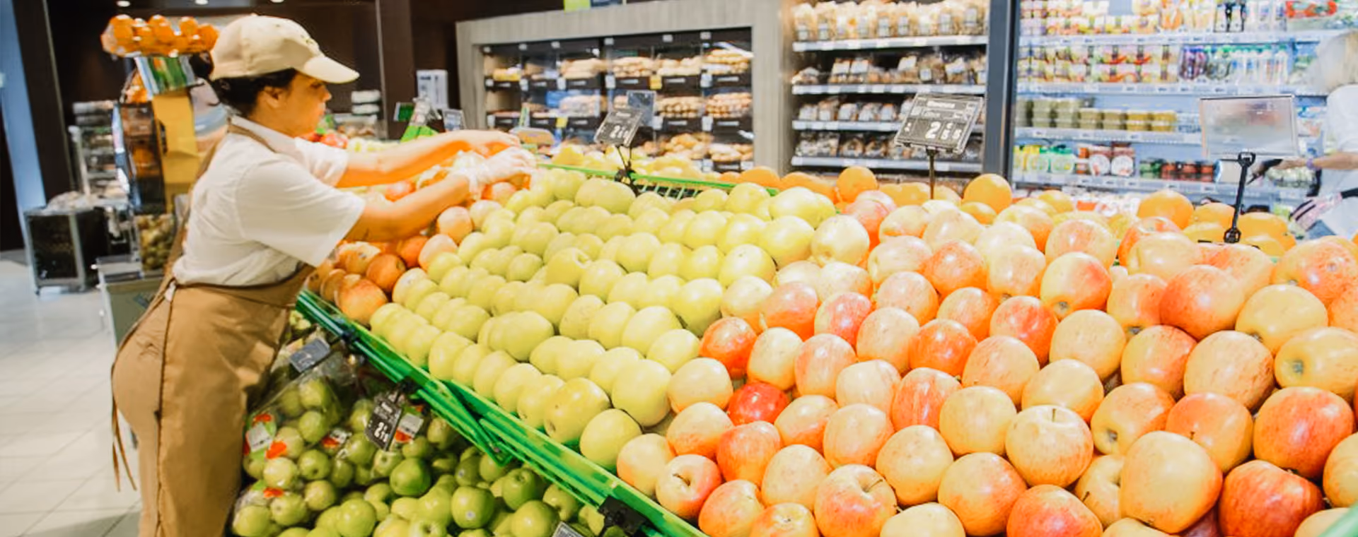 Ladenangestellter arrangiert Äpfel, die in einem gut beleuchteten Lebensmittelgeschäft ausgestellt werden.