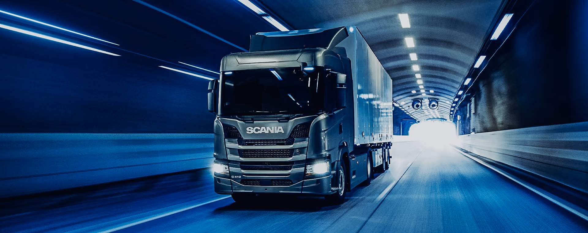 Scania G410 truck driving through a brightly lit tunnel.