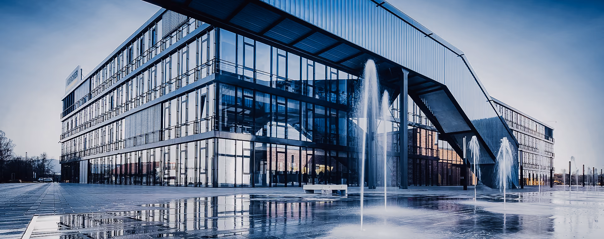 Modern Kärcher glass building with reflective windows and multiple water fountains in front.