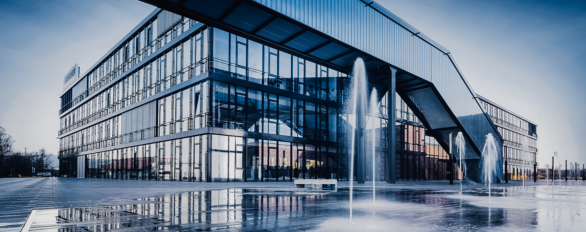 Modernes Kärcher-Glasgebäude mit reflektierenden Fenstern und mehreren Wasserfontänen davor.