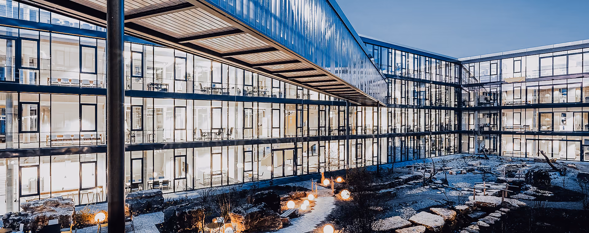 Modern Kärcher office building with large glass windows overlooking an illuminated courtyard with stone paths.